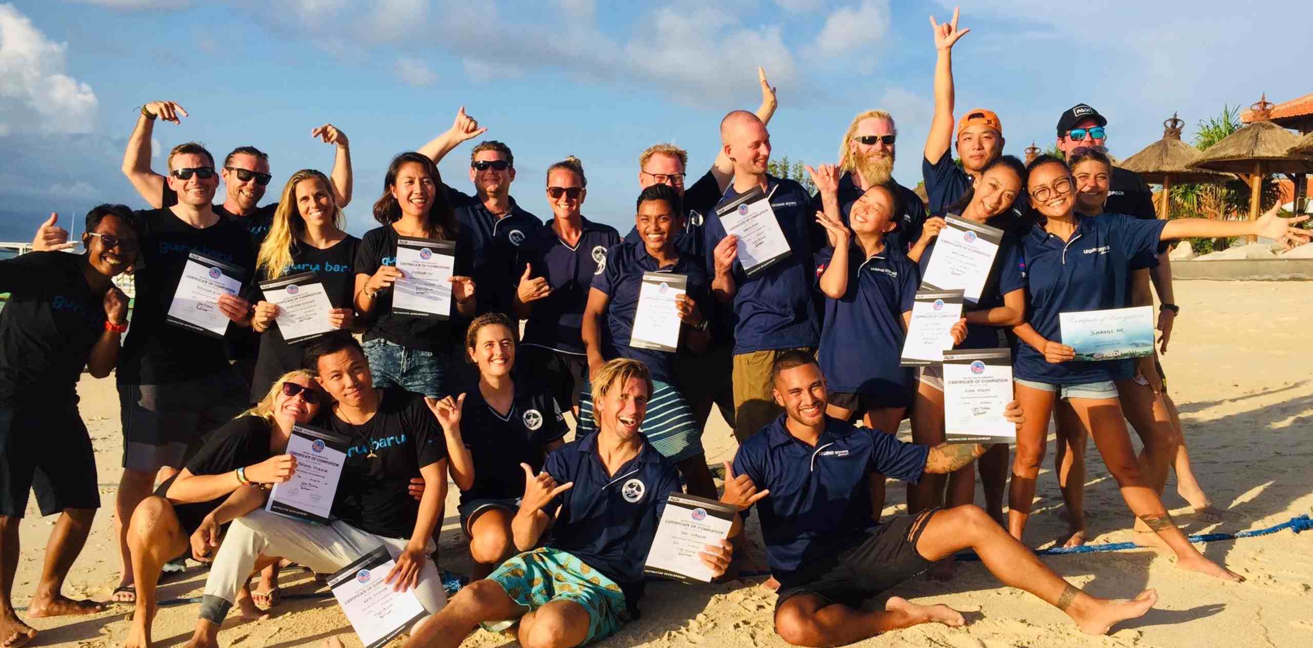 一群人在Nusa Lembongan海滩举证书合影庆祝，有人比“冲浪手势”和张开手臂欢呼。